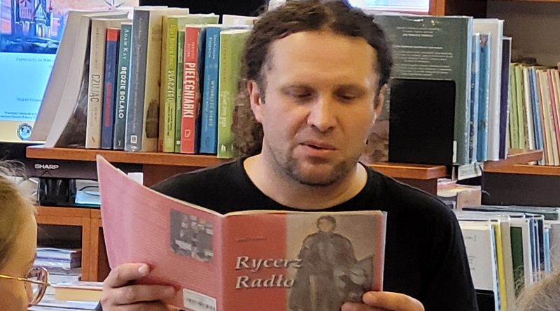 Rysownik Szymon Teluk czyta książeczkę o rycerzu, w tleksiążki